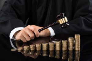 Judge's hands striking gavel in front of stacked coins on desk.