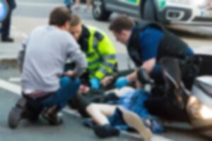 Paramedics and firefighters administering first aid to motorcycle accident victims on the street. Blurred background.
